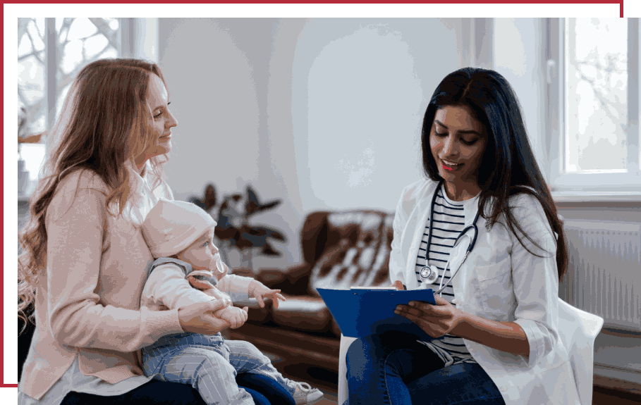 A woman with a baby in her arms sits before a laptop, illustrating the family-oriented approach of Bonneville Family Practice.