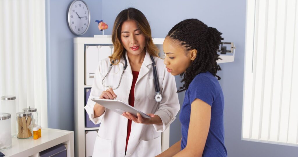 A doctor with a stethoscope reviews a tablet with a patient in a medical office.