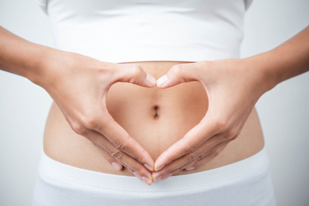 Hands form a heart shape over a person's abdomen against a white background.