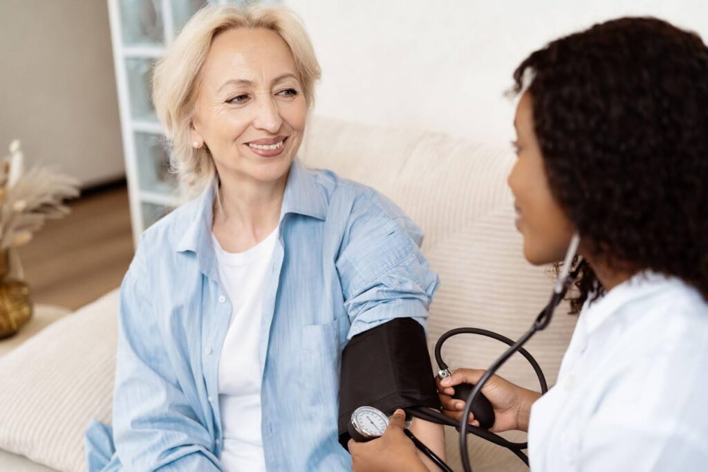 A woman sits on a couch as a doctor measures her blood pressure