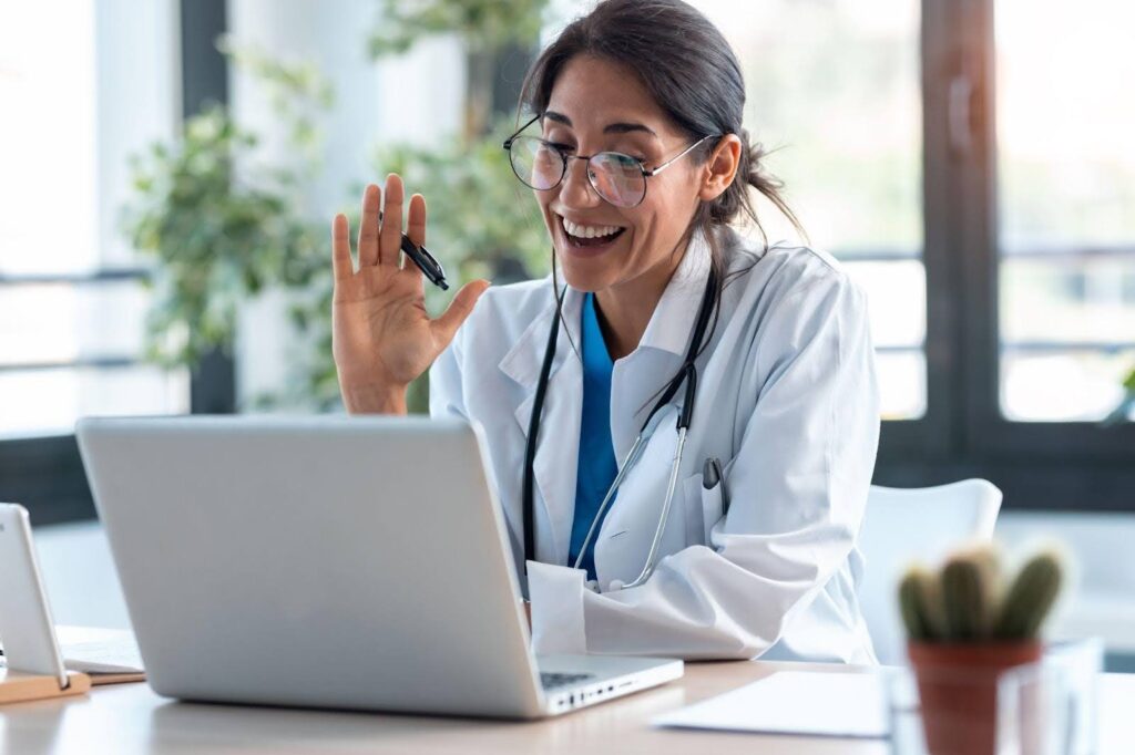 A woman in a lab coat is engaged in a conversation on her laptop focused and attentive
