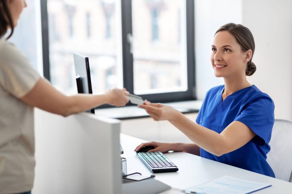 A woman in scrubs hands a credit card to another woman indicating a payment