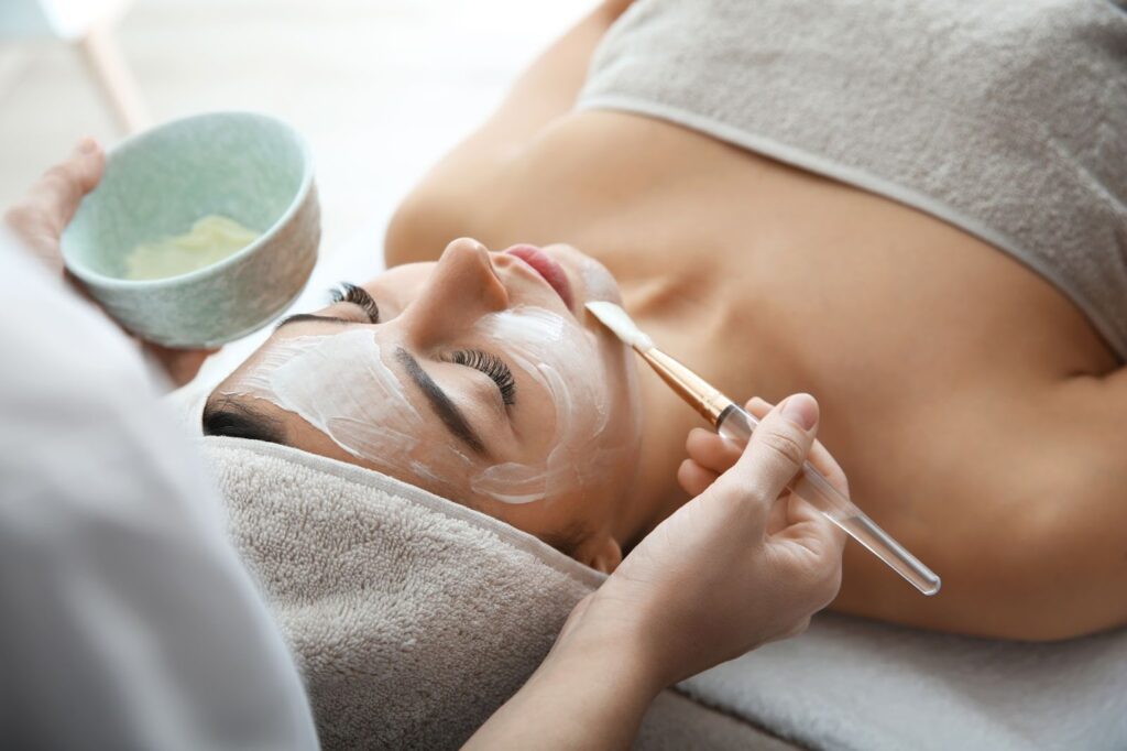A person receiving a facial treatment with a cream mask applied by a professional using a brush.