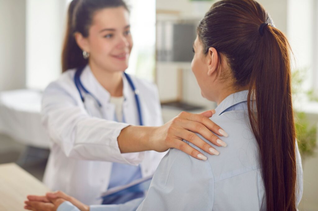 Female doctor placing a reassuring hand on her patient's shoulder during a medical consultation.
