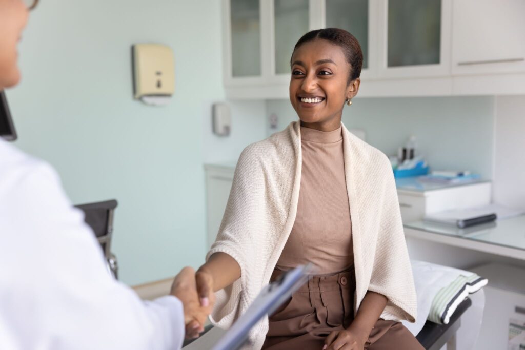 Smiling patient shaking hands with a doctor during a consultation in a medical office.